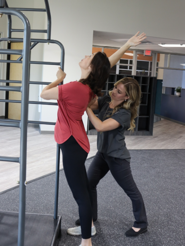 A therapist positioning the shoulder of a woman as she reaches overhead.