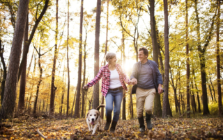 Active senior couple with dog on a walk in a beautiful autumn forest, running.