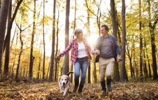 Active senior couple with dog on a walk in a beautiful autumn forest, running.