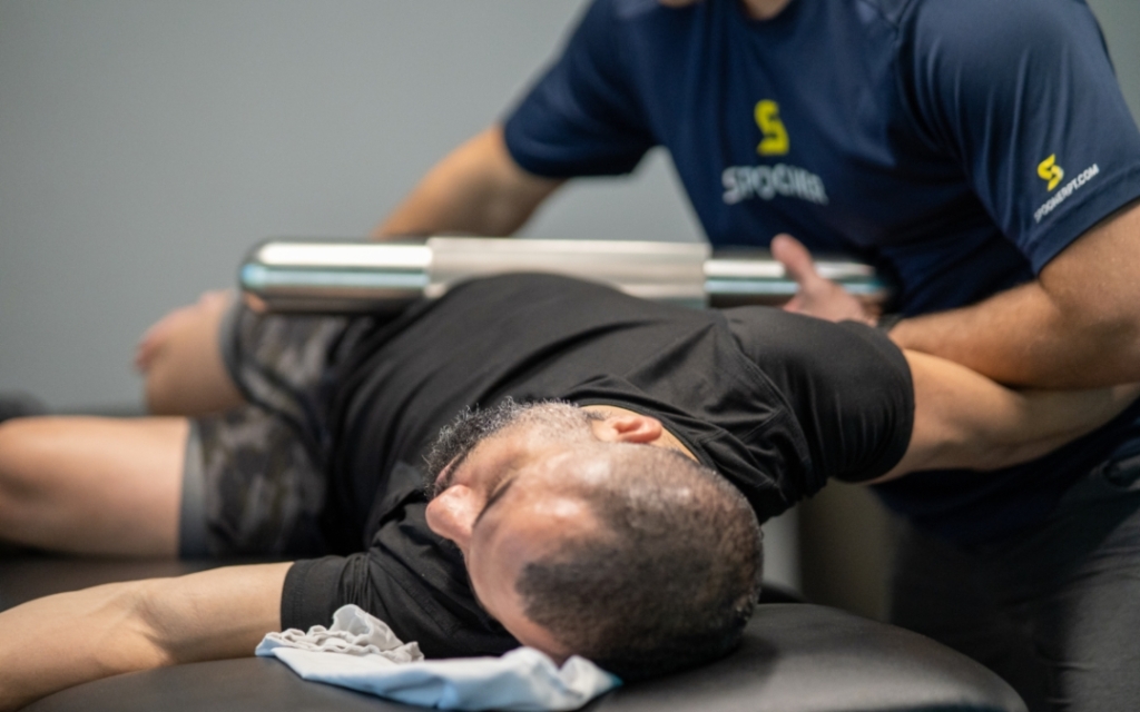 Image of a man laying on a table having his hip tempered with a with a roller.