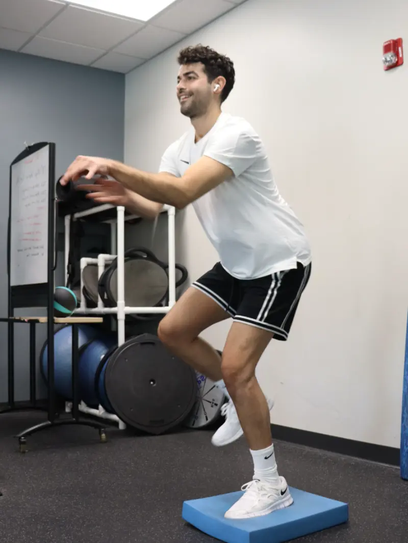 Image of an ACL patient on blue balance pad throwing a ball.