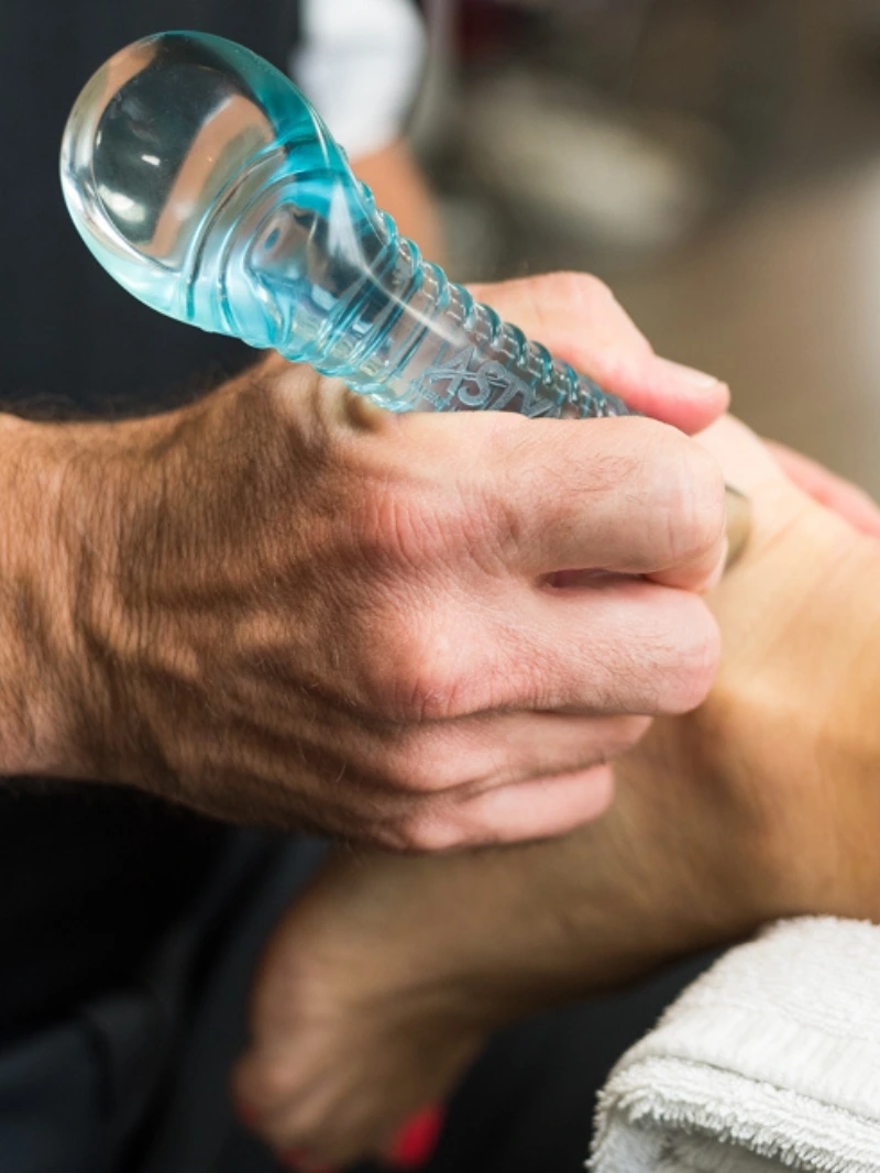 Image of an astym tool being used on an ankle of a patient.