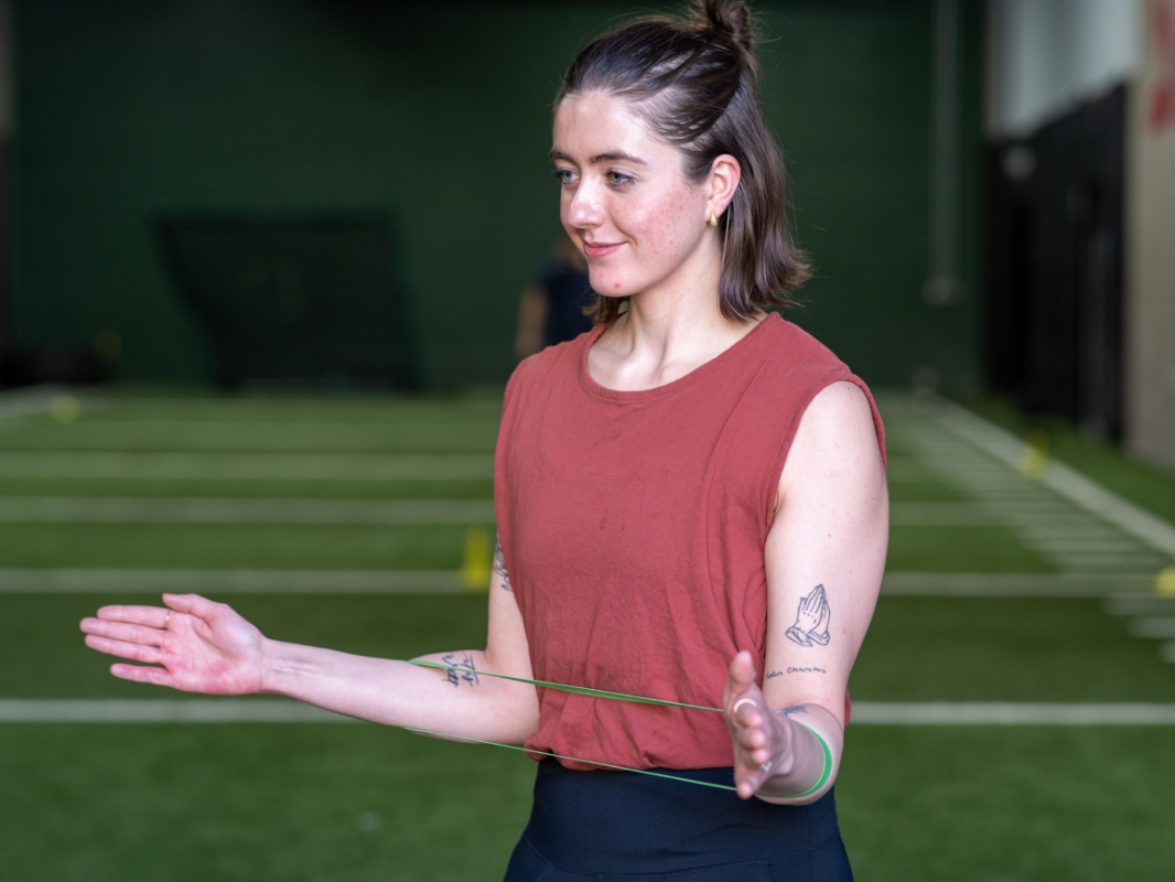 Woman with a tension band around her forearm, elbows bent at 90 degrees and spread apart, in the banded external rotation ending position.