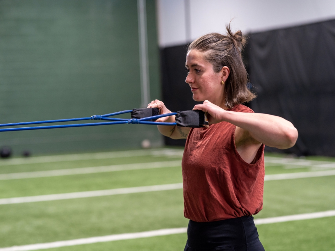 Image of a woman doing the face pull exercise with the tension rope pulled to her chest with elbows raised.