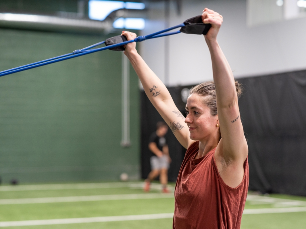 Image of a woman doing the face pull exercise in the end position with the tension rope raised above her head with arms straight up.