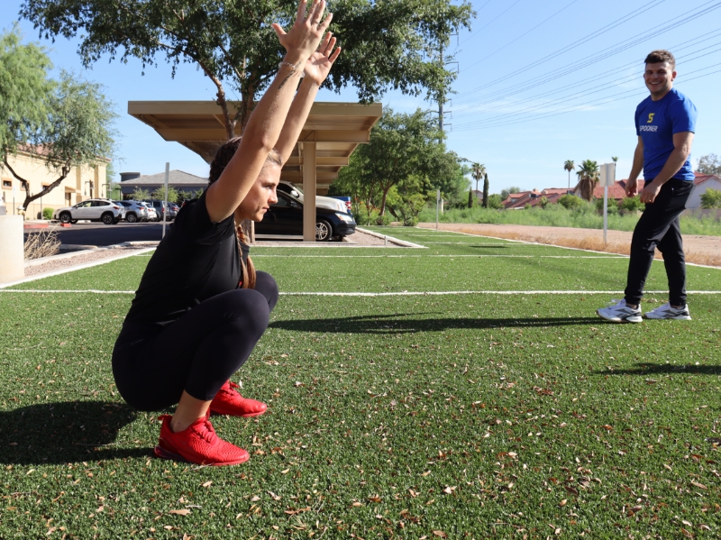 Image of a woman squatting and stretching both arms into the air.