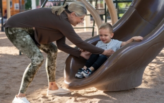 Feature image of an older woman bending down to to pick up a young boy off the bottom of a slide.