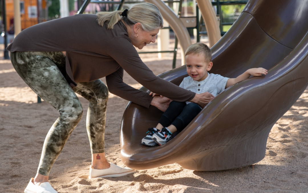 Feature image of an older woman bending down to to pick up a young boy off the bottom of a slide.