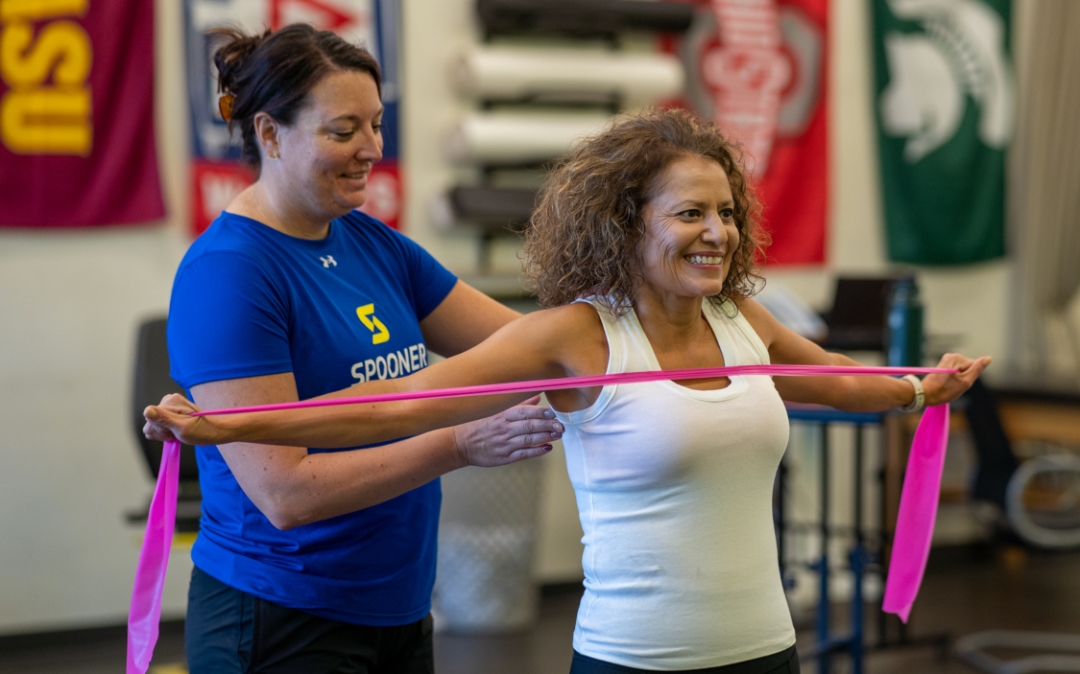 Image of Jenna Salber and a middle aged woman with her arms extended, stretching out a pink resistance band.