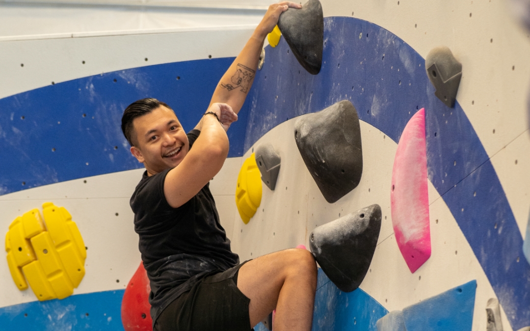 Staying on the wall blog feature image of a man smiling and hanging on to a rock climbing wall.