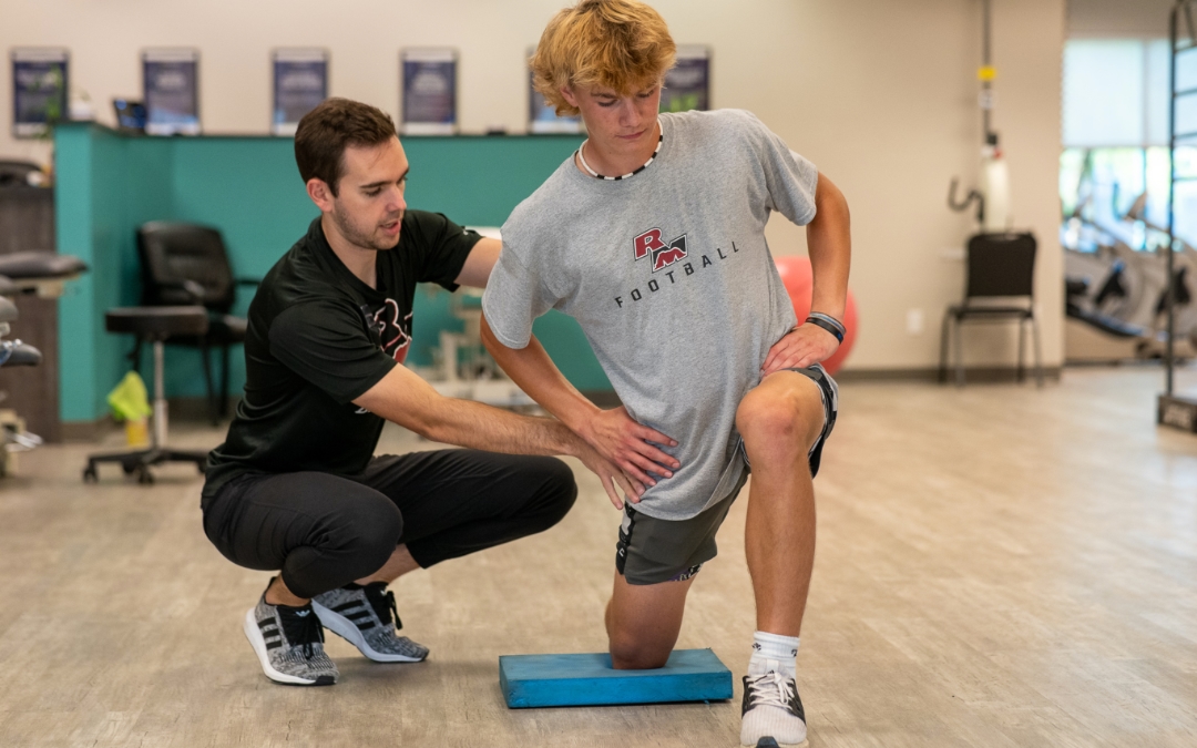 Treating the growing athlete feature image of Brian Bettner helping a male, teen athlete kneeling on a blue pad.