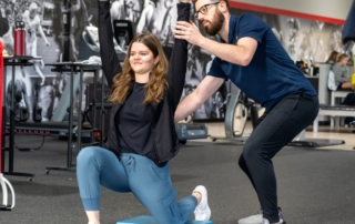 A physical therapist adjusts the position of a patient doing overhead raises.